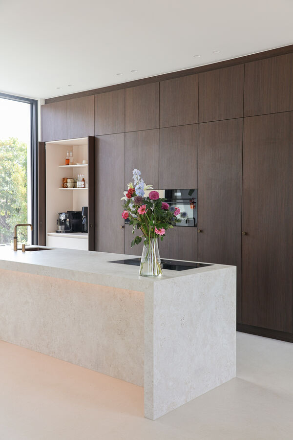 Keuken met donker houten kastenwand en stenen keukeneiland met bloemenboeket, realisatie van Ilwa Keukens